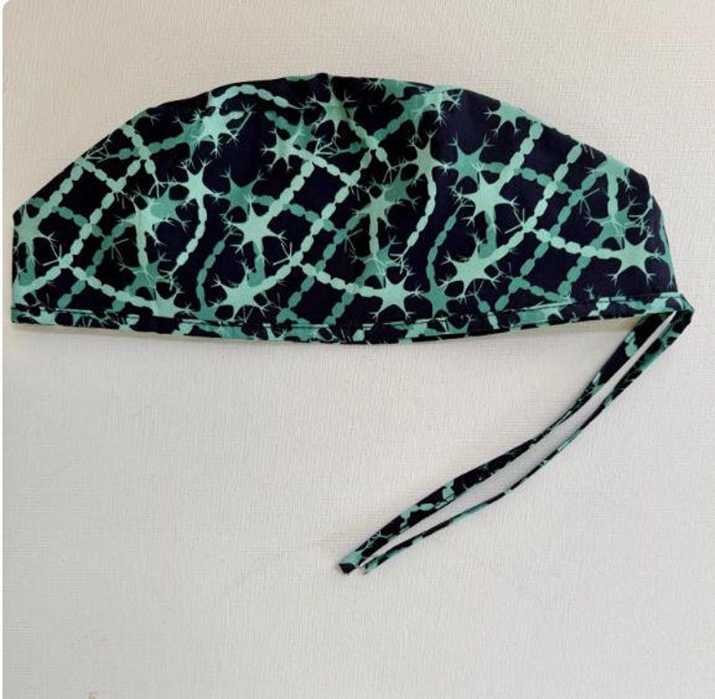May include: A navy blue surgical scrub cap with a repeating pattern of interconnected teal neuron-like shapes. The cap has a tie closure at the back for an adjustable fit. The fabric is a soft, lightweight material.