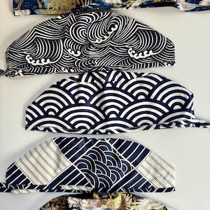 May include: Five different patterned surgical caps with ties. The patterns include cranes, waves, and geometric shapes in shades of blue and white.