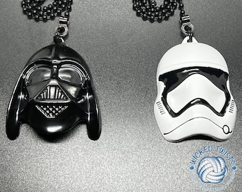 May include: Two black metal chains with a Darth Vader and a Stormtrooper helmet charm. The charms are black and white and have a metallic finish. The chains are attached to the charms with a metal ring. The charms are hanging from a white background.