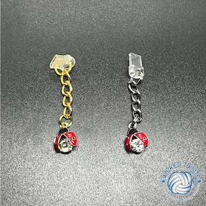 May include: Two ladybug charms with clear rhinestone accents. One charm has a gold chain and the other has a silver chain. Both charms have a clear plastic loop at the top.