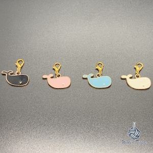May include: Four whale charm pendants in black, pink, blue, and white. Each charm has a gold lobster clasp.