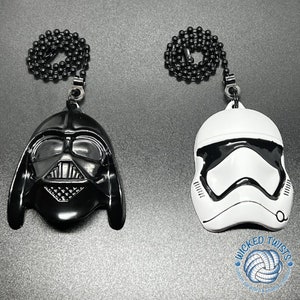 May include: Two black metal chains with a Darth Vader and a Stormtrooper helmet charm. The charms are black and white and have a metallic finish. The chains are attached to the charms with a metal ring. The charms are hanging from a white background.
