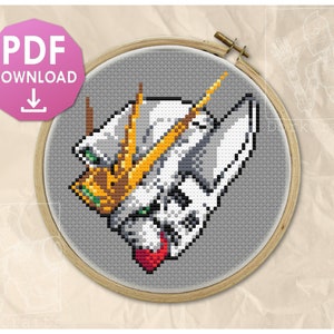 May include: A cross-stitch pattern in a wooden embroidery hoop featuring a pixelated robot head design. The robot is white, gray, and yellow with green accents and a red chin piece, set against a gray background. A pink PDF DOWNLOAD icon is visible.
