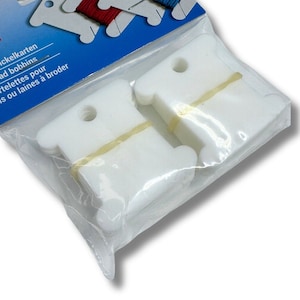 Könnte beinhalten: Eine Packung mit 30 weißen Garnwickelkarten, zusammengehalten von einer transparenten Kunststoffverpackung. Die Packung hat ein blau-weißes Etikett mit dem Text "Frym" und "Thread bobbins". Die Karten dienen zum Ordnen von Garn für Näh- und Stickprojekte.