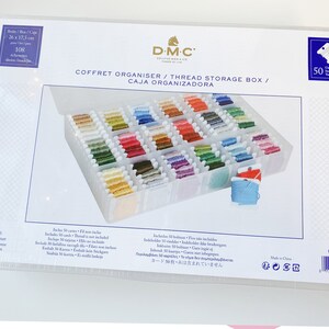 May include: A clear plastic thread storage box with a white lid. The box contains numerous spools of colorful embroidery floss. The box is labeled "COFFRET ORGANISER / THREAD STORAGE BOX / CAJA ORGANIZADORA" and measures 10.2 x 6.9 inches.