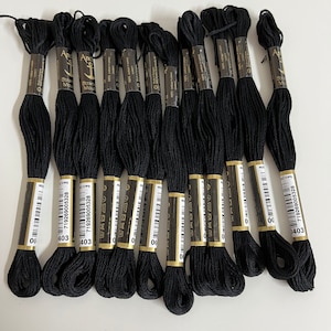 May include: A collection of black embroidery floss skeins, each with a label. The labels display the brand name "Anchor" and the color number "403". The floss is made of 100% cotton.