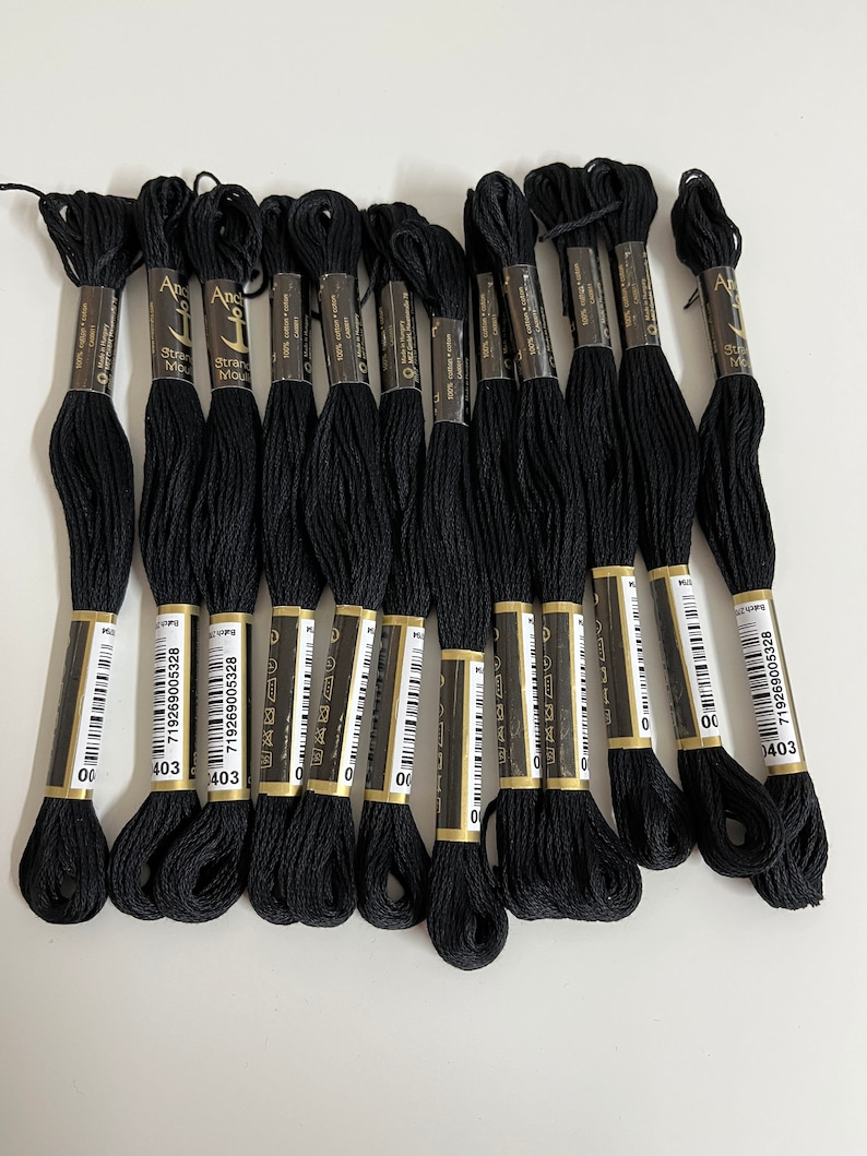 May include: A collection of black embroidery floss skeins, each with a label. The labels display the brand name "Anchor" and the color number "403". The floss is made of 100% cotton.