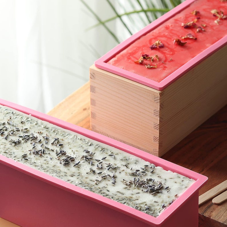 May include: Two pink silicone molds for making soap. One mold is filled with a light green soap with dried lavender buds. The other mold is filled with a pink soap with dried rose petals.
