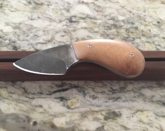 May include: A small, handmade knife with a Damascus steel blade and a wooden handle. The handle is secured with two small screws.