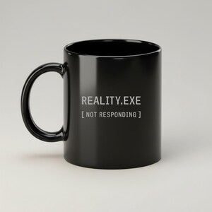 Könnte beinhalten: Schwarze Keramik-Tasse mit gebogenem Henkel. Die Tasse zeigt den Text "REALITY.EXE [NOT RESPONDING]" in weißer, serifenloser Schrift. Die Tasse hat eine glänzende Oberfläche und ist für heiße oder kalte Getränke geeignet.