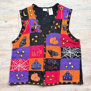 May include: A sleeveless knit vest featuring a patchwork design in black, orange, purple, and red. The vest displays embroidered Halloween motifs including pumpkins, bats, spiders, webs, stars, houses, and candy corn, with text reading Happy Halloween and Trick or Treat.