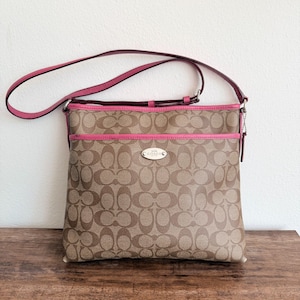 May include: A tan and brown monogram print crossbody bag with bright pink leather trim and a matching pink adjustable shoulder strap. The front features a horizontal zippered pocket and a silver-toned metal plaque with the text COACH NEW YORK.