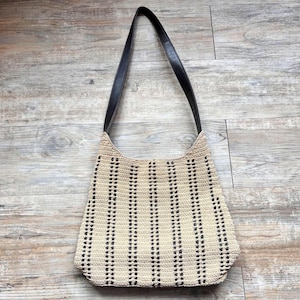 May include: A beige and black woven shoulder bag with a black leather strap. The bag features a vertical striped pattern and a rounded shape, perfect for everyday use.