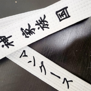 May include: White martial arts belt with black embroidered text that reads "Black Belt" and "A-1 Karate".