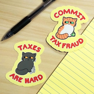 May include: Two yellow stickers with black outlines and red text. One sticker features a cartoon cat with orange and white fur, holding money and the text "Commit Tax Fraud". The other sticker features a cartoon cat with gray fur, holding money and the text "Taxes Are Hard".