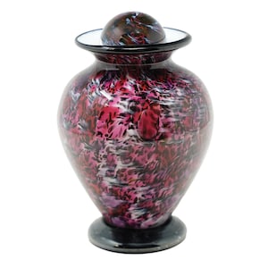 Peut inclure: Une urne funéraire en verre rose et noir avec un motif en spirale. L'urne a un couvercle avec un bord noir.