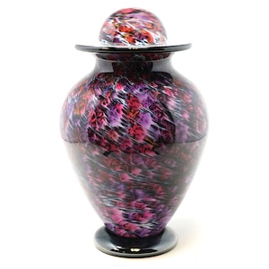 May include: A glass urn with a lid, featuring a swirling pattern of pink, purple, and black. The urn has a round base and a wide opening.