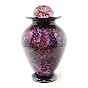 May include: A glass urn with a lid, featuring a swirling pattern of black, pink, and white. The urn has a round base and a wide mouth.