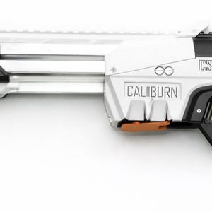 May include: A white and black toy rifle with orange and blue accents. The word "CALIBURN" is printed on the side. The toy rifle has a long barrel and a handle.