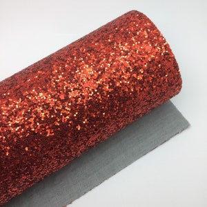 Op de afbeelding: Een rol oranje glitterstof met een fijne, glinsterende textuur. De stof is opgerold en het einde is zichtbaar.