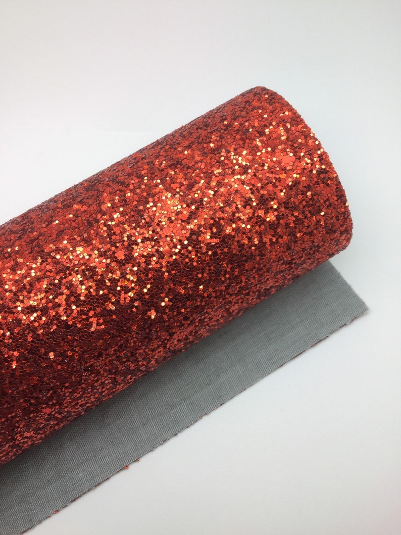 Op de afbeelding: Een rol oranje glitterstof met een fijne, glinsterende textuur. De stof is opgerold en het einde is zichtbaar.