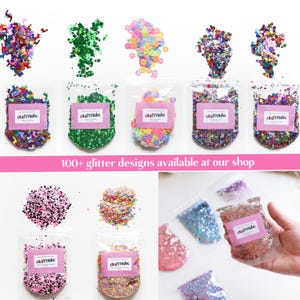 May include: Assortment of colorful glitter in small resealable bags. The glitter is in various shapes and sizes, including stars, hearts, and circles. The bags are labeled "CRAFTYRIFIC". The text "100+ glitter designs available at our shop" is displayed below the bags.