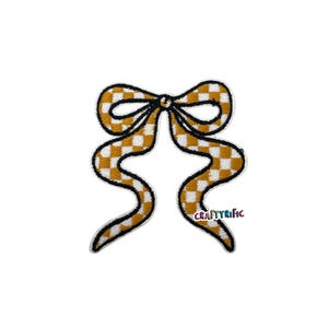 May include: A fabric patch in the shape of a bow. The bow features a yellow and white checkered pattern with a black outline. The text "CRAFTYRIFIC" is visible on the lower right side.