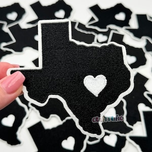 May include: Black felt outline of the state of Texas with a white heart in the center. The patch is surrounded by other similar patches.