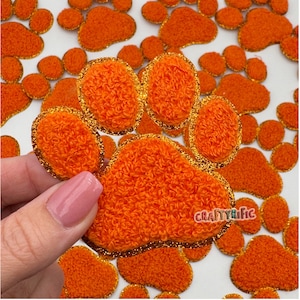 May include: Orange felt paw print patches with a gold glitter trim. The patches are about 2 inches in diameter.
