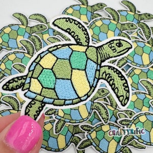 May include: A collection of colorful embroidered iron-on patches featuring sea turtles with a patchwork shell design. The turtles are outlined in black and have a green, blue, and yellow shell.