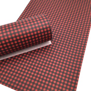 May include: A roll of faux leather fabric featuring a red and black buffalo plaid check pattern. The material has a textured surface and a white backing visible on the rolled edge, displaying a consistent grid design across the entire sheet.