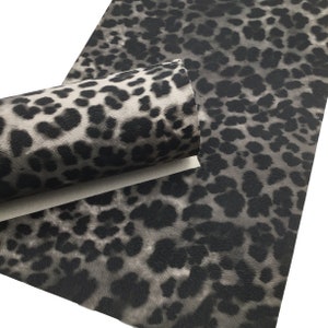 May include: Black and white leopard print faux leather fabric. The fabric has a textured, furry look.