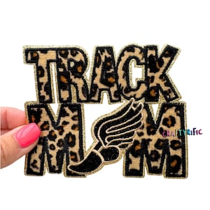 May include: A leopard print patch with the words "TRACK MOM" in black outlined letters with gold glitter trim. A black and gold track and field symbol is featured in the design.