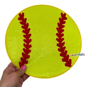 May include: A yellow softball with red stitching. The softball is made of sequins and has a yellow border.