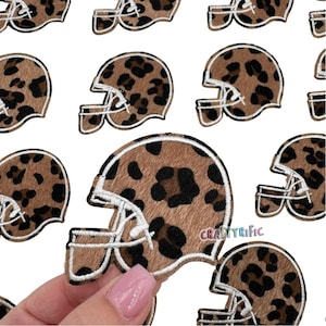 May include: A set of 10 brown and black leopard print iron-on patches shaped like football helmets. The patches have white stitching around the edges.