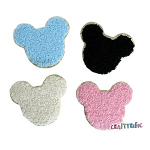 May include: Four fuzzy fabric Mickey Mouse head appliques in blue, black, white, and pink. Each applique has a gold glitter outline.
