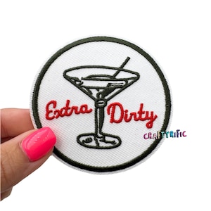 May include: Round white embroidered patch with a black border. The patch features a black martini glass with a red "Extra Dirty" text. The patch is held by a hand with a pink nail polish.