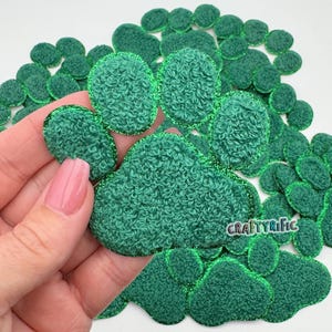 May include: Green fuzzy paw print fabric patches with a glittery green outline. The patches are arranged in a paw print shape.