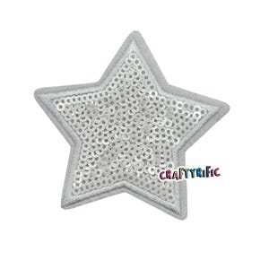 May include: A silver star-shaped patch covered in white sequins. The patch is outlined in white thread.