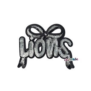 May include: A sequined patch with the word "LIONS" in silver sequins, outlined in black. The word is connected to a black sequined bow. The patch has a white background.