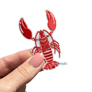 May include: Embroidered red lobster patch with white accents. The lobster is detailed with visible claws, body segments, and antennae. The patch has a white border and the text "CRAFTYrific" is visible.
