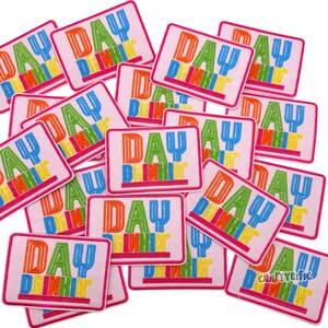 Pu&ograve; includere: Una collezione di toppe rettangolari rosa con la scritta "DAY DRINKIN'" ricamata in lettere colorate. Le toppe hanno un bordo rosa e sono sparse nell'immagine.