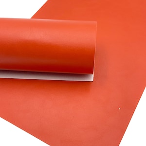 May include: A roll of bright orange faux leather fabric. The fabric has a textured surface and is rolled up with the edges tucked in.