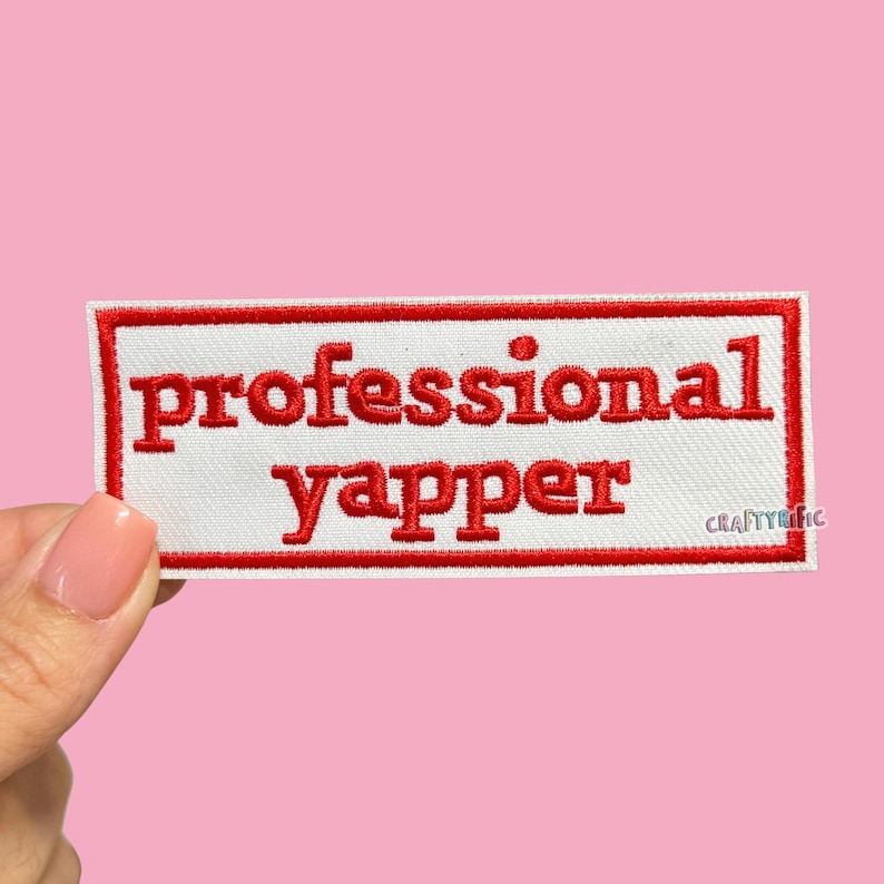 Pu&ograve; includere: Una toppa rettangolare bianca con bordo rosso e le parole "professional yapper" ricamate in rosso. La toppa &egrave; mostrata su uno sfondo rosa.