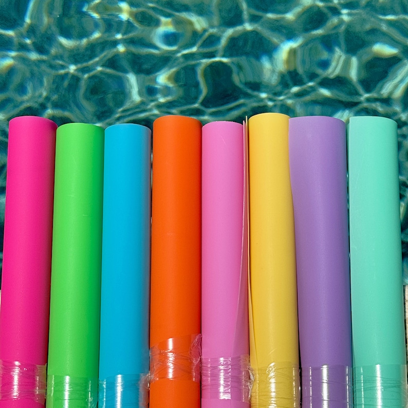 May include: A set of nine pool floats in various colors, including pink, green, blue, orange, yellow, and purple. The floats are all cylindrical and have a smooth, shiny surface.