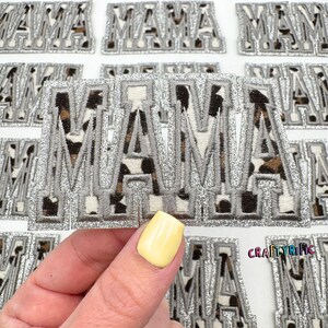 May include: A set of silver glitter iron-on patches that spell out "MAMA" with a leopard print background.