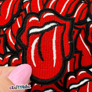 May include: A close-up of a red embroidered patch with a white tongue sticking out, resembling a famous rock band logo. The patch is surrounded by other similar patches.