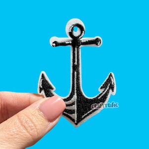 May include: Black and white embroidered anchor patch with the text "CraftyRific" on a blue background. The anchor has a classic design with a curved shank and flukes. The patch is held by a person's hand.