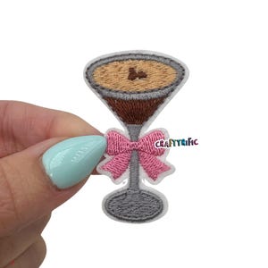 May include: Embroidered iron-on patch of a martini glass with a brown drink and a pink bow. The patch is on a white background.