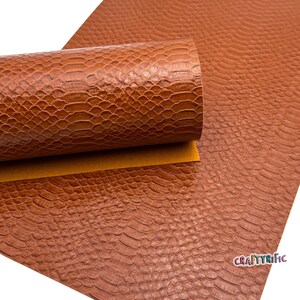 May include: A sheet of brown faux leather with a snake skin pattern. The leather is rolled up and the pattern is visible on both the rolled and unrolled portions.